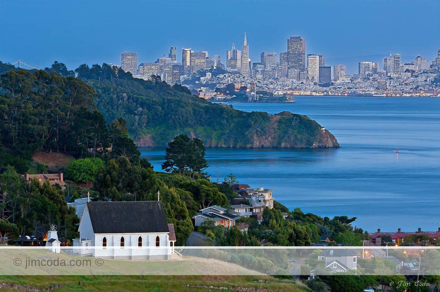 This is a photo of old St. Hilary's Church in the town of Tiburon at dusk with Angel Island, Alcatraz and the San Francisco skyline in the background..